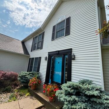 Two-story house with clean white vinyl siding and blue front door after professional washing