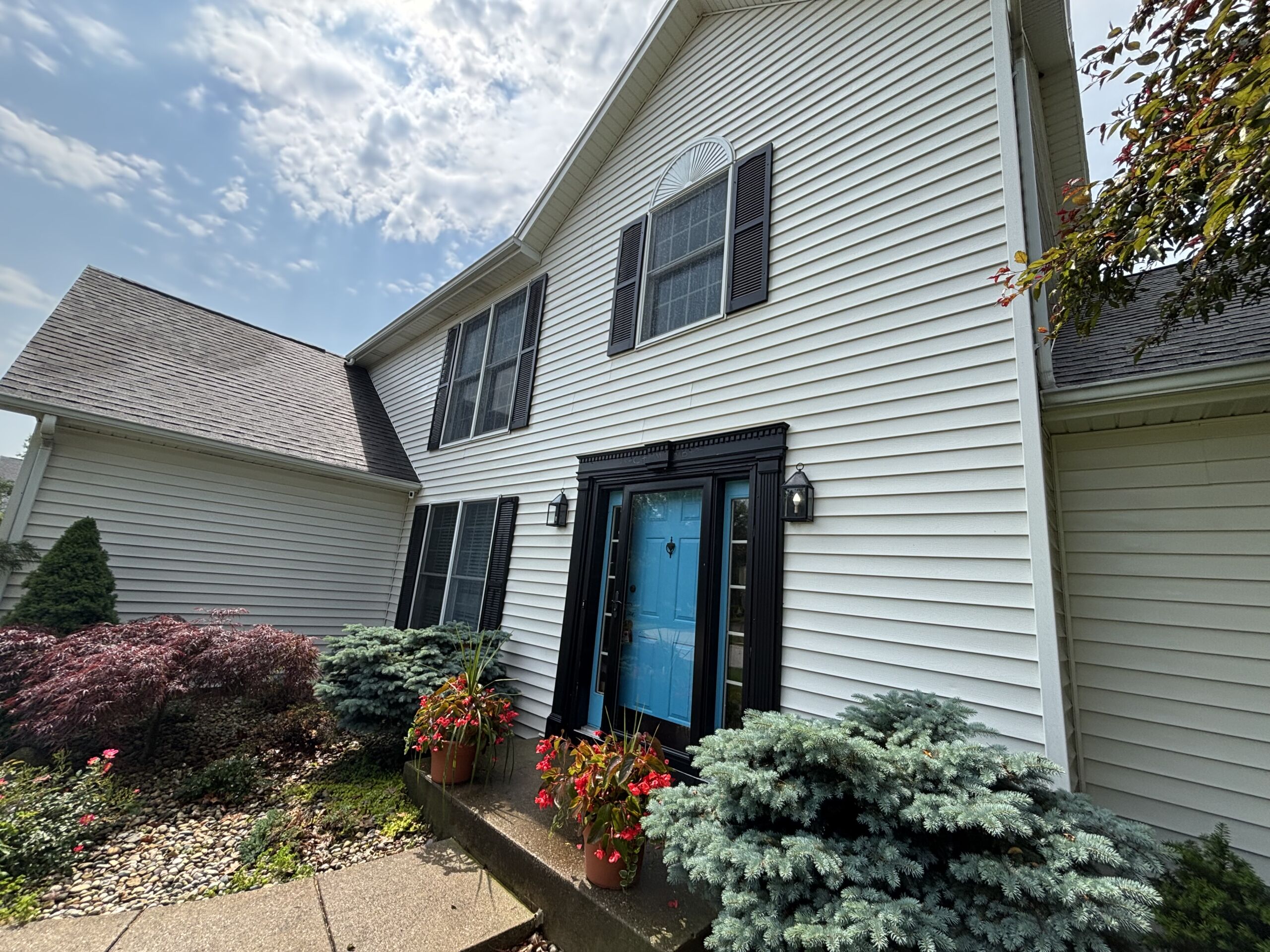 Two-story house with clean white vinyl siding and blue front door after professional washing