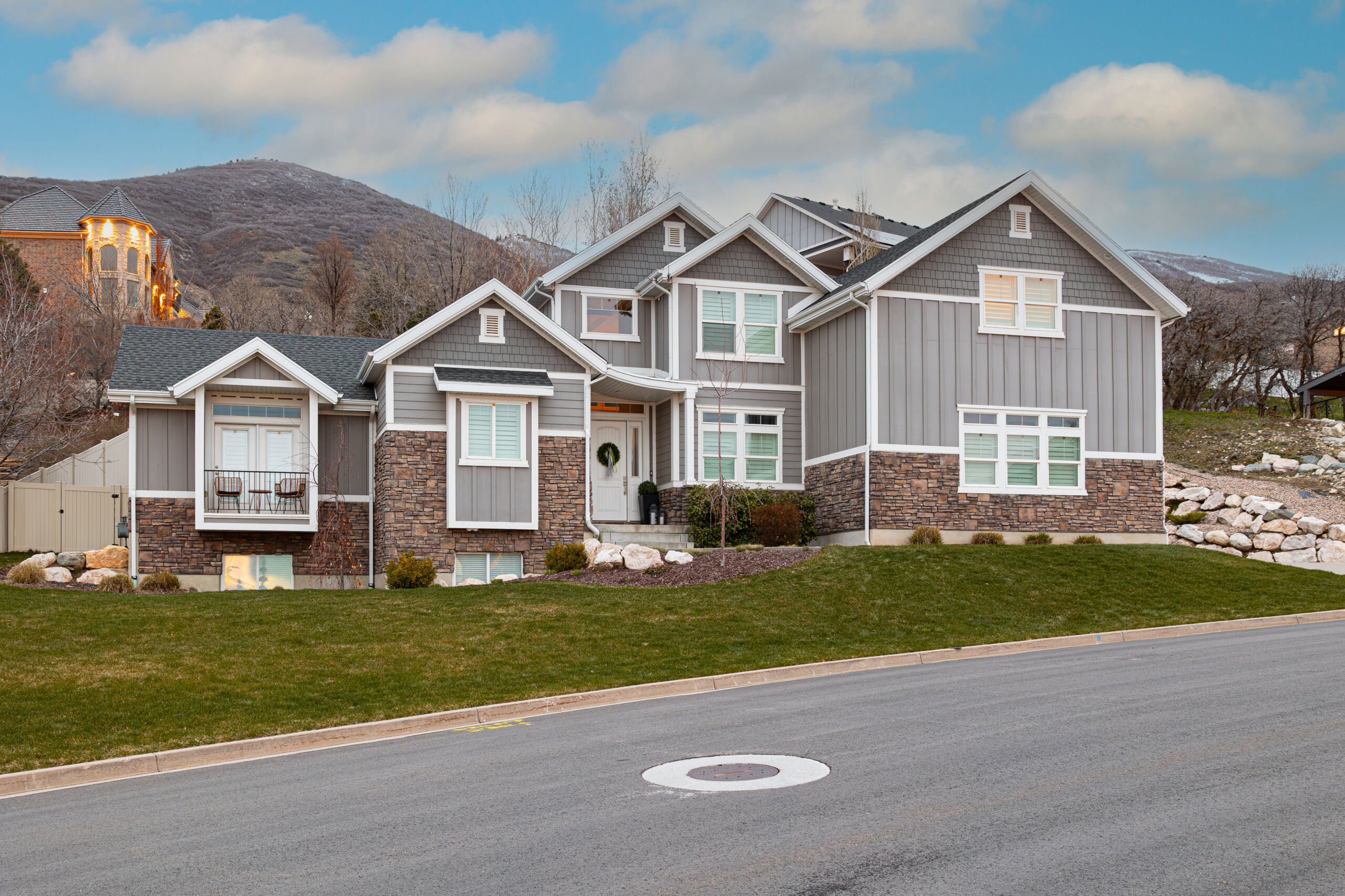Copy of FARMINGTON LANDSCAPE-100 Large gray craftsman home with stone accents and a wreath on the front door set against a hillside backdrop