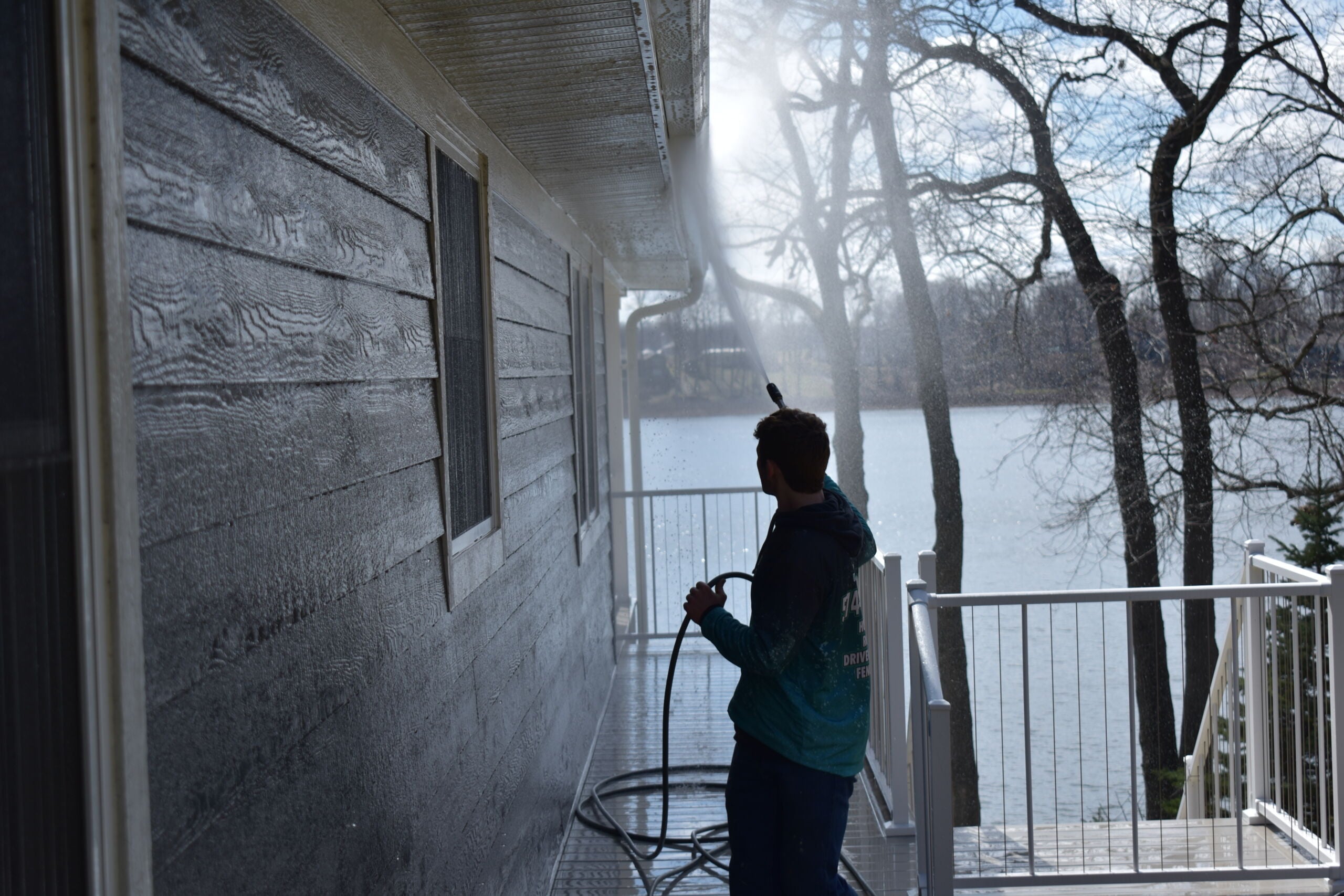 Prime & Shine technician soft washing algae-covered siding on a lakefront home from the deck