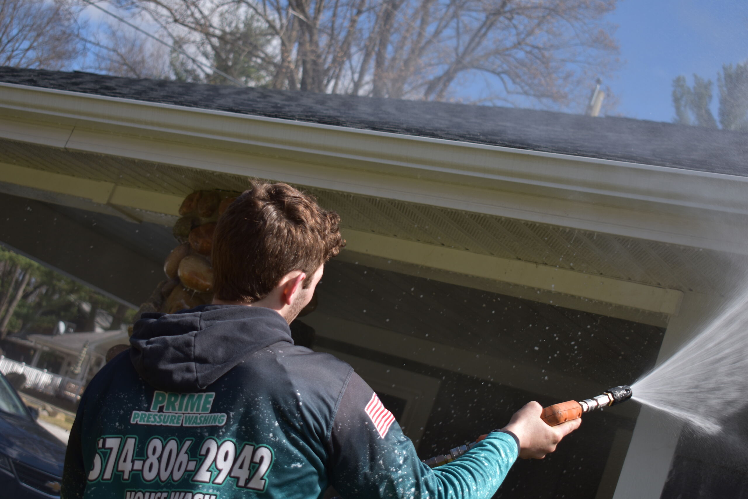 Prime Pressure Washing technician spraying soffit and eaves of a house exterior