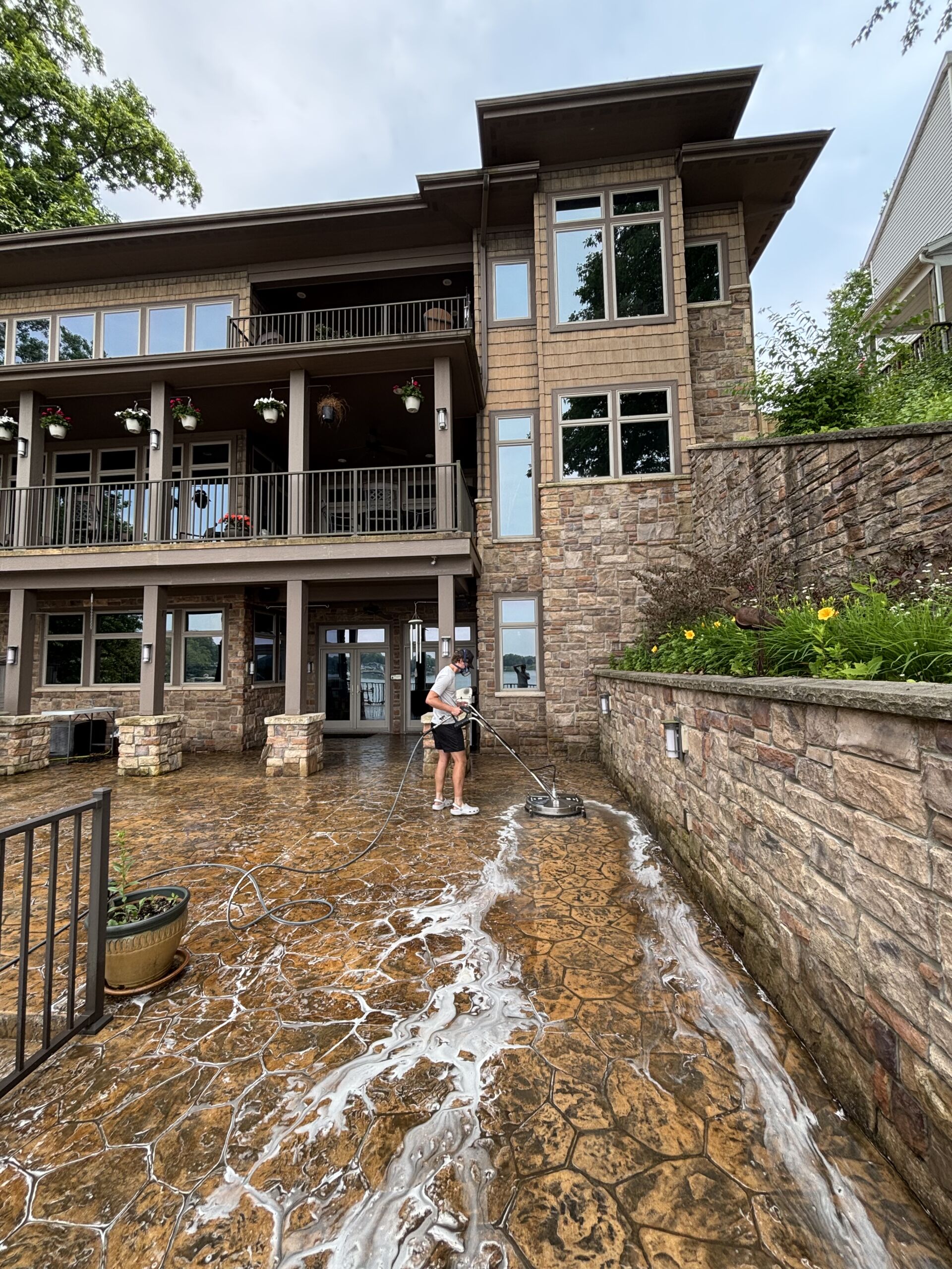 Technician surface cleaning a soapy stamped concrete patio at a large lakefront stone home