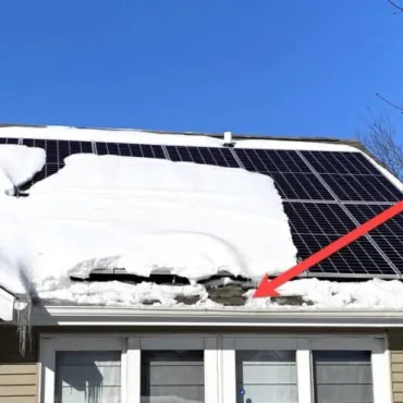 Roof solar panels partially covered in snow with ice dam damage highlighted by red arrow