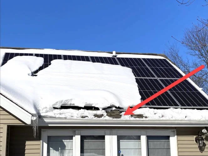 Roof solar panels partially covered in snow with ice dam damage highlighted by red arrow