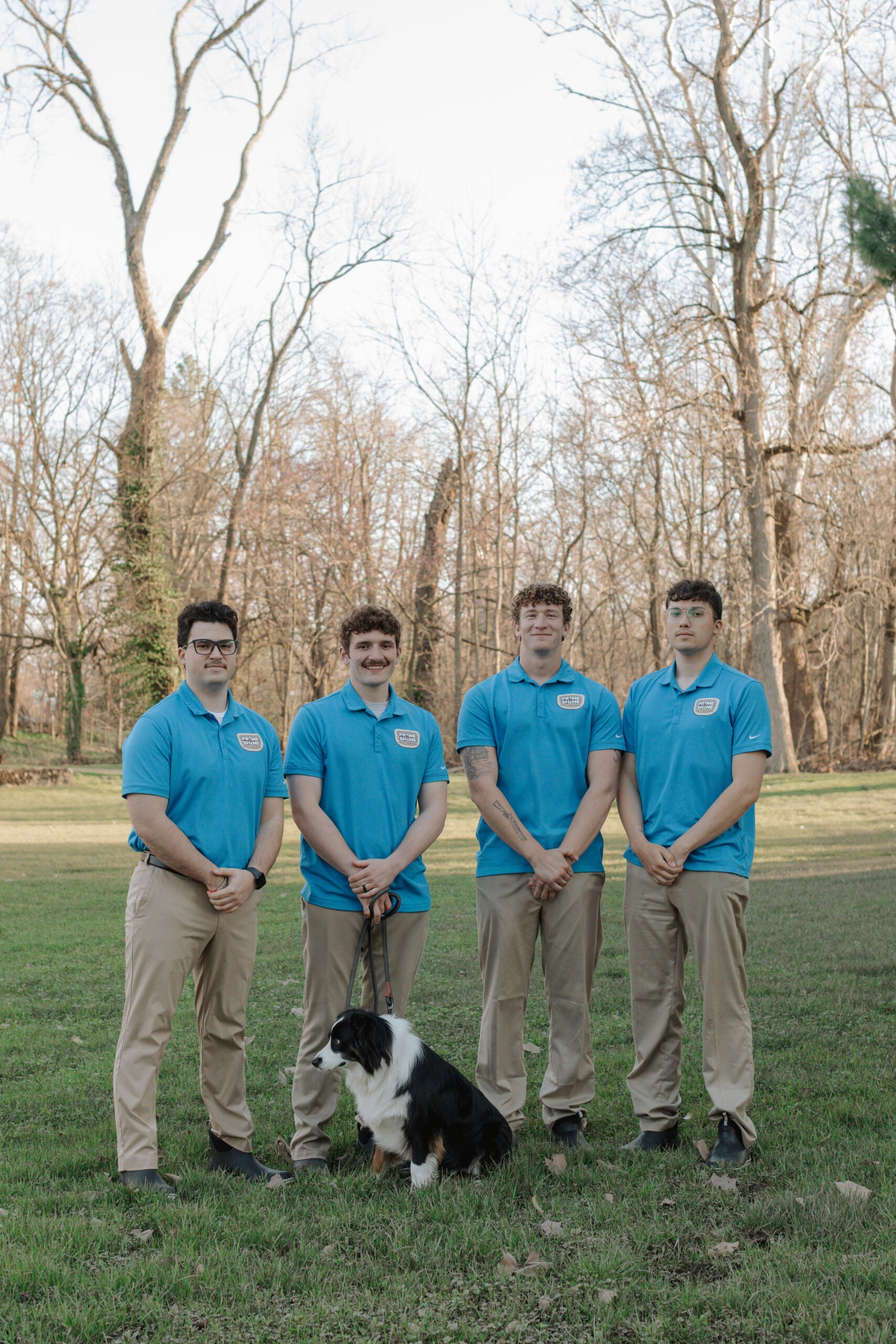 Prime & Shine team of four technicians in blue polo uniforms posing outdoors with company dog