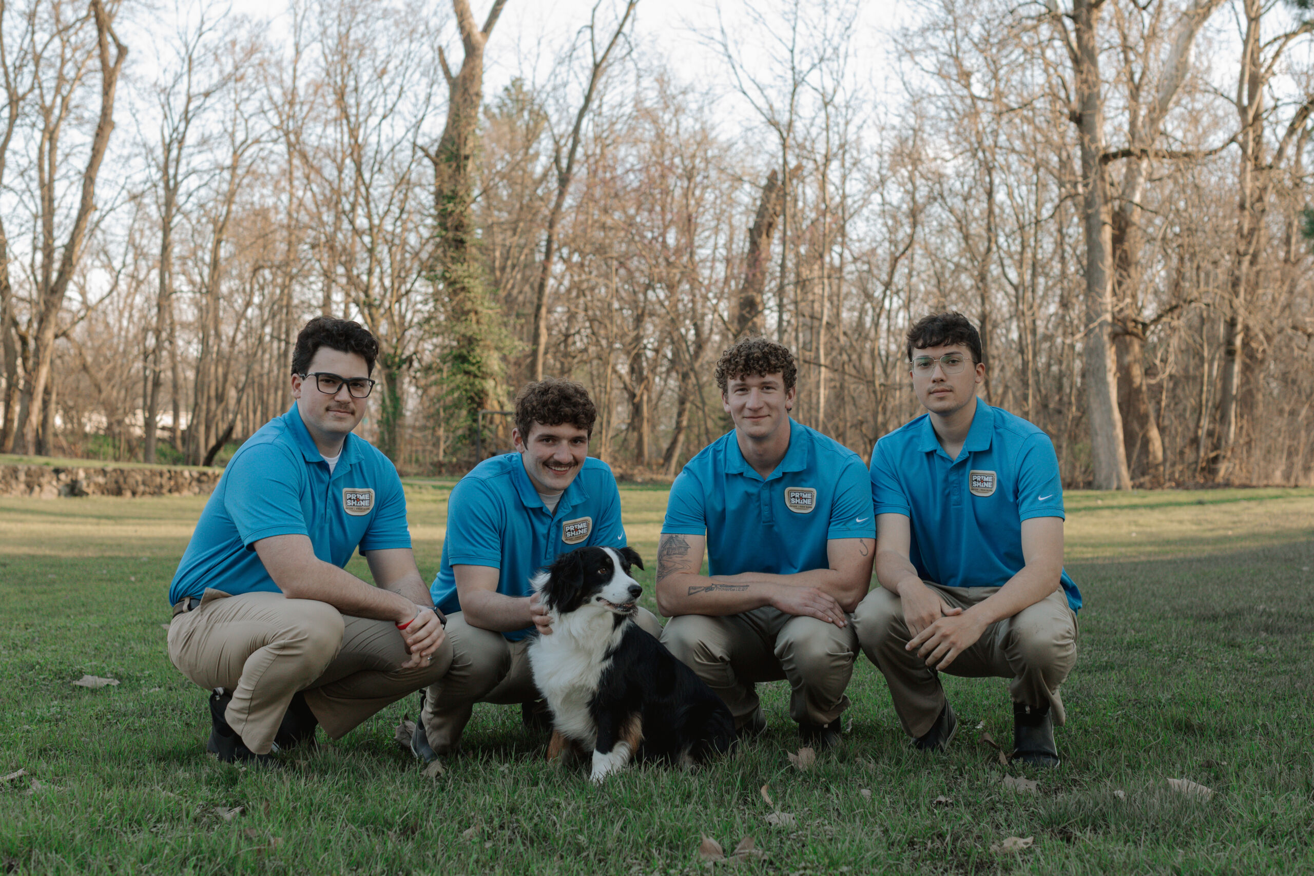 Prime & Shine team of four technicians in blue polo uniforms posing outdoors with company dog