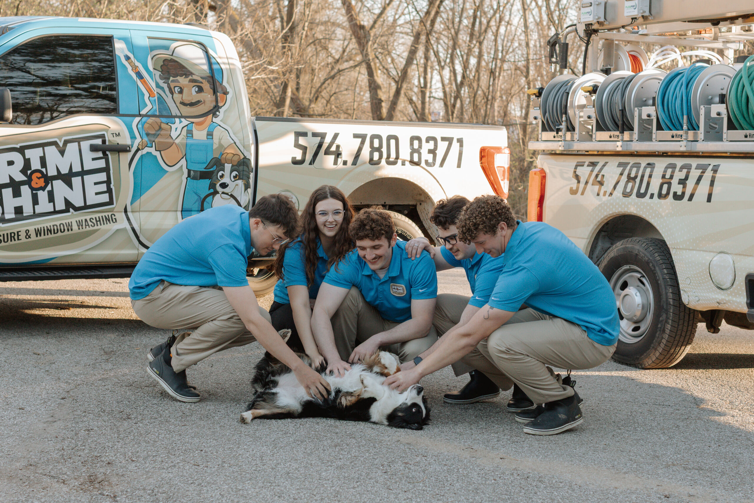 Prime & Shine team of five petting company dog beside branded work trucks